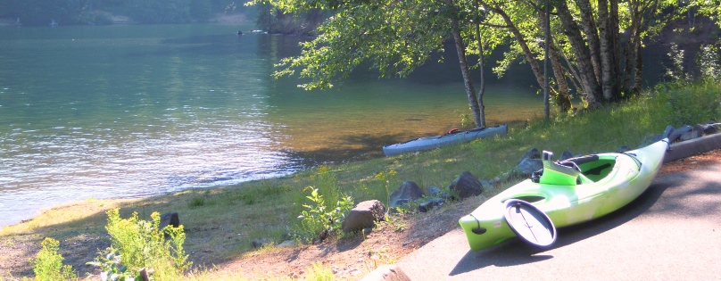 A lake side photo with the lake, a green kayak and trees